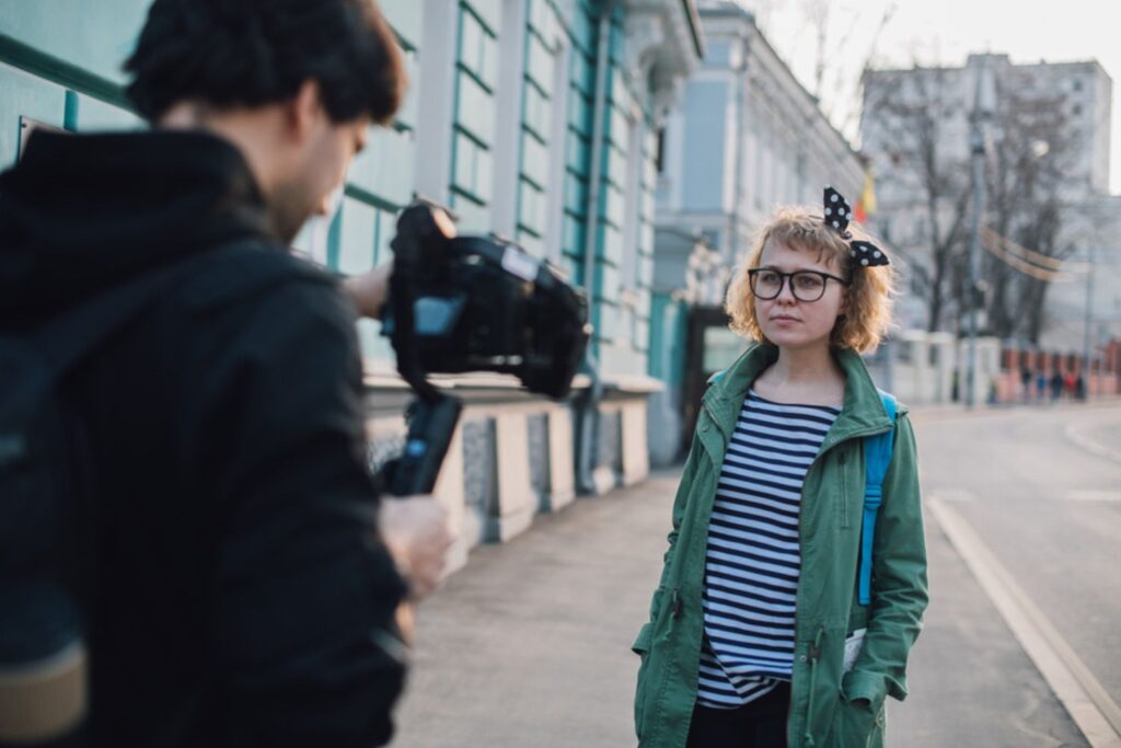 Immagine con un operatore video che si appresta a girare una scena con la tecnica da film del piano sequenza, riprendendo una ragazza in contesto urbano